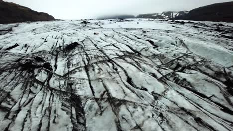 Aerial-landscape-view-of-people-hiking-on-the-textured-ice-of-Sólheimajökull-glacier,-Iceland,-in-summer