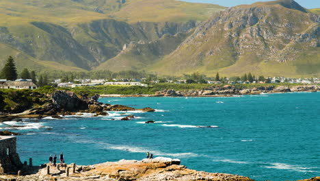 Scenic-Hermanus-coastline-with-beautiful-mountains-in-the-background---tourists-doing-whale-watching-from-the-rocks