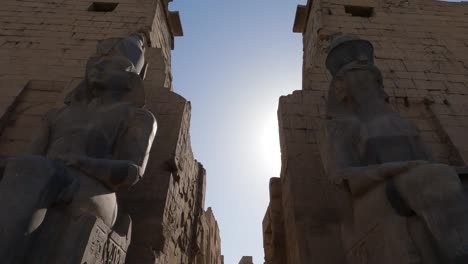 Huge-sitting-Statues-in-Karnak-complex,-Tilt-down-from-the-blue-sky-revealing-Statues-and-historical-site