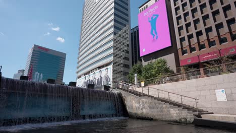 Cheonggyecheon-Stream-Wasserfall-Und-Große-öffentliche-Werbung-Digitale-Wand-Plakatwand-Spielen-Airpods-Werbespot-An-Schönen-Sommertagen,-Während-Leute-Am-Cheonggye-Quadrat-In-Seoul-City-Spazieren-Gehen