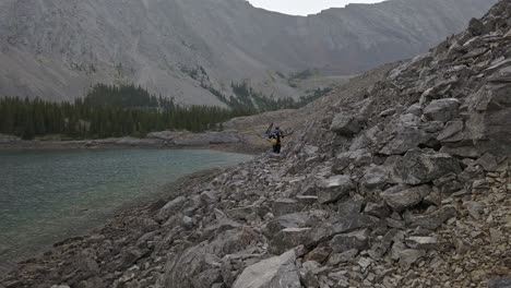 Biker-carrying-bike-in-mountains-in-rain-by-lake-and-rocks-followed-Rockies-Kananaskis-Alberta-Canada
