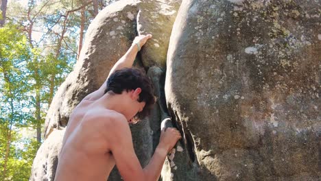 close-up-of-shirtless-teenage-boy-climbing-up-crag-boulder-in-fontainebleau