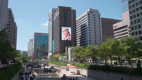 People-Travel-at-Cheonggyecheon-Stream-Park-in-Seoul-City,-Swarowski-and-Audi-Commercial-Advertisement-on-Huge-Wall-Digital-Display-at-Downtown