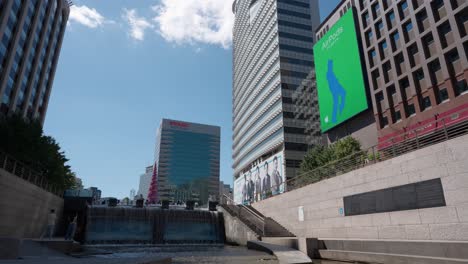 Huge-Public-Advertisement-Digital-Wall-Display-playing-Airpods-Commercial-near-Cheonggyecheon-Stream-Park-on-Summer-Beautiful-Day-in-Seoul-City,-South-Korea