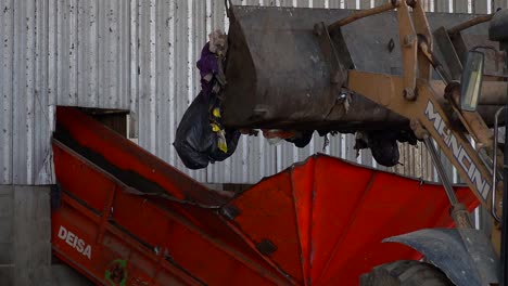 The-bucket-of-a-bulldozer-dumps-garbage-onto-a-conveyor-belt-inside-a-waste-processing-facility