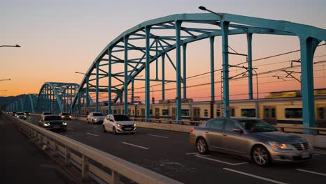 Dongjak-bridge-against-a-sunset-sky-with-Seoul-metro-train-traveling-from-Dongjak-subway-station-and-many-cars-on-city-highway,-South-Korea