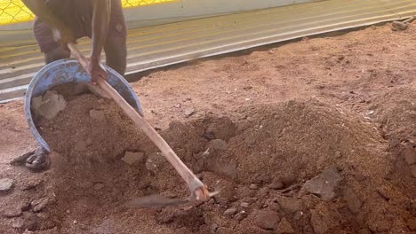 Using-a-digging-hoe-as-a-tool,-a-laborer-must-manually-remove-dirt-and-place-it-in-a-steel-bowl