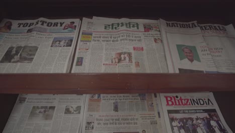 Schwenk-Nach-Unten-Auf-Verschiedene-Indische-Zeitungen,-Die-Im-Holzregal-Ausgestellt-Sind
