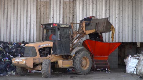A-bulldozer-dumps-garbage-onto-a-conveyor-belt-inside-a-waste-processing-facility