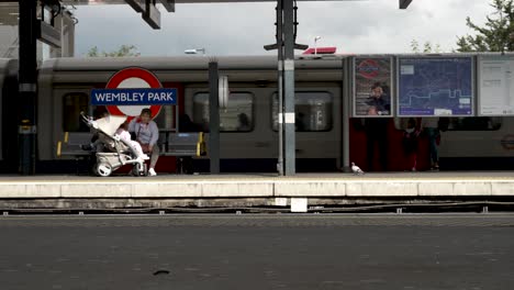 Metropolitan-Train-Pulling-Into-Wembley-Park-Station-Platform-With-Commuters-Waiting