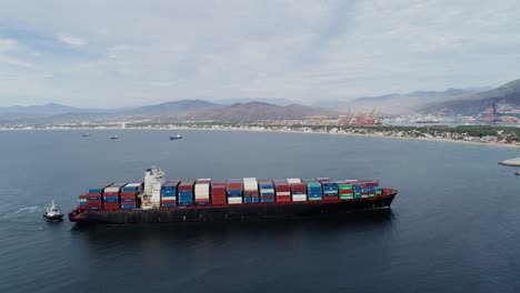 Aerial-view-following-a-big-cargo-ship,-moving-towards-the-Manzanillo-Port,-in-Mexico