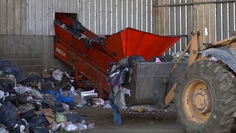 A-bulldozer-approaches-a-conveyor-belt-to-dump-garbage-inside-a-waste-processing-facility