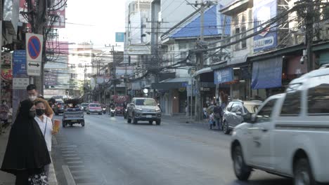 Blick-Auf-Die-Lokale-Straße-Von-Bangkok-An-Der-Bushaltestelle-Zwischen-Hochhäusern-Mit-Menschen,-Die-Auf-Den-Bus-Warten