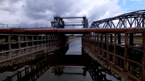 Forward-aerial-movement-through-canal-underneath-steel-draw-bridge-access-drive-for-large-cargo-ships-to-pass-by-at-river-IJssel