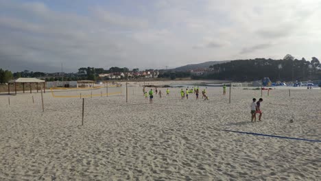 Adult-beach-soccer-coach-with-children-watches-the-activity-among-the-volleyball-nets-in-flashy-colored-T-shirts-one-summer-morning,-shot-blocked