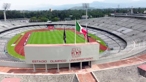 Reveal-of-the-University-Olympic-Stadium-With-the-Mexican-Flag-Between-the-Pumas-Flag-and-the-UNAM-Flag-Waving-over-the-Entrance-in-Mexico-City