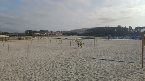 Adult-beach-soccer-coach-for-children-marks-with-his-foot-in-the-sand-between-the-volleyball-nets-with-brightly-colored-shirts-one-summer-morning,-shot-blocked