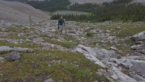 Hiker-walking-up-mountain-with-lake-and-forest-circling-Rockies-Kananaskis-Alberta-Canada