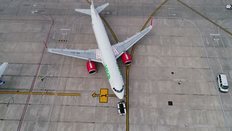 Push-back-tug-assisting-a-plane-backwards-at-departure,-at-a-airport---aerial-view