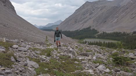 Hiker-walking-up-mountain-with-lake-and-forest-Rockies-Kananaskis-Alberta-Canada