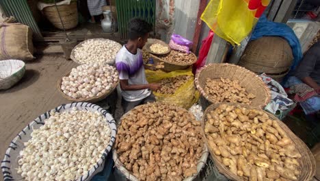 Market-Stall-Trader-Surrounded-By-Large-Baskets-Of-Garlic-And-Ginger-In-Bangladesh