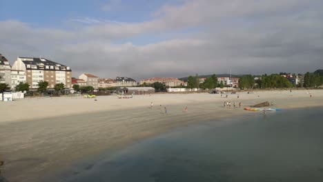 Menschen-Und-Kinder-Führen-An-Einem-Bewölkten-Morgen-Freizeitsportaktivitäten-In-Gruppen-Im-Sand-Des-Strandufers-Durch,-Blockierte-Panoramaaufnahmen,-Porto-novo,-Galizien,-Spanien