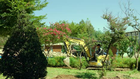 Mini-Digger-Working-In-A-Garden-or-Park-In-Summer---wide-shot