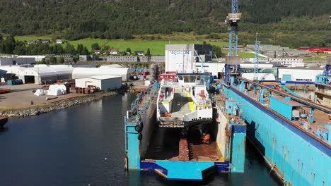 Ferryboat-ship-is-inside-floating-drydock-for-maintenance-at-Westcon-yards-at-Olensvag-Norway---Backward-moving-aerial-with-yard-logo-on-building-in-background