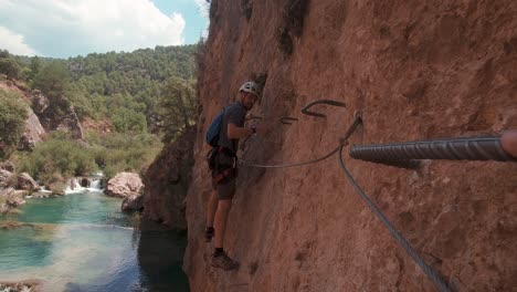 POV-action-cam-young-climber-in-Via-Ferrata-rock-wall-over-beautiful-river-and-waterfall