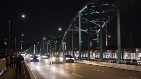 People-walking-on-Dongjak-bridge-at-night,-cars-traffic,-Seoul-metro-train-travel-on-railroad-bridge-towards-Dongjak-subway-station,-photographers-take-pictures-of-downtown-view-with-Han-river
