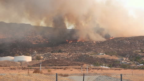 A-shot-of-the-raging-Fairview-wildfire-coming-dangerously-close-to-an-evacuated-farm-house,-the-fire-continues-to-burn-the-dry-arid-landscape-leaving-behind-a-path-of-destruction,-Hemet,-California
