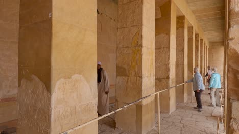 Tour-Guide-Going-Under-Barrier-At-The-Mortuary-Temple-Of-Hatshepsut-On-Sunny-Day-With-Tourists-Walking-Past