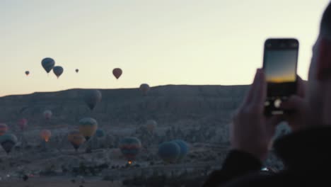Man-taking-photos-of-hot-air-balloons-with-phone-at-sunrise