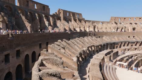 Tilt-down-Inside-of-Famous-Landmark-in-Rome,-Stunning-Colosseum-with-tourists-on-Bright-sunny-day