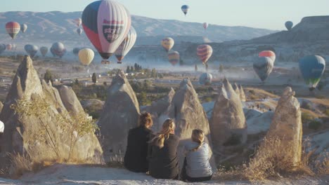 Girlfriends-sitting-watching-balloons-over-Cappadocia-at-sunrise
