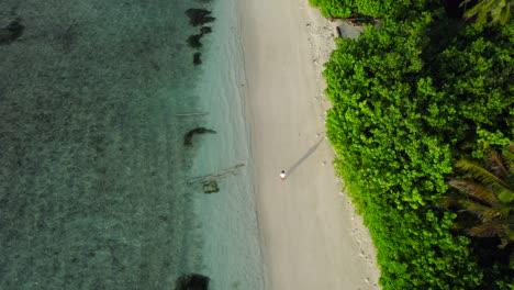 Man-walking-alone-through-tropical-beach-at-sunrise-in-Dhigurah-island,-Maldives