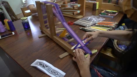 Purple-and-white-yarn-being-pressed-and-fitted-using-traditional-Asian-weaving-methods,-filmed-over-shoulder-as-close-up