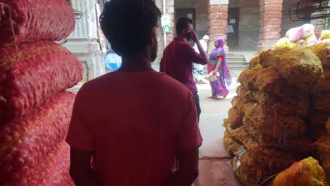 POV-Walking-Behind-Trader-Past-Piles-Of-Stacked-Onion-Sacks-In-Storehouse-In-Bangladesh