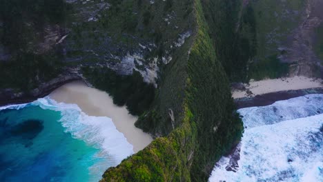 Beautiful-cinematic-aerial-shot-of-exotics-mountains,-crystal-clear-blue-water-and-waves-hitting-the-beach-of-Nusa-Penida-Kelingking