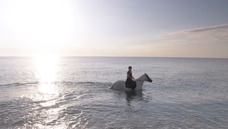 Woman-with-helmet-riding-horse-inside-water-of-ocean-at-sunset-,slow-motion