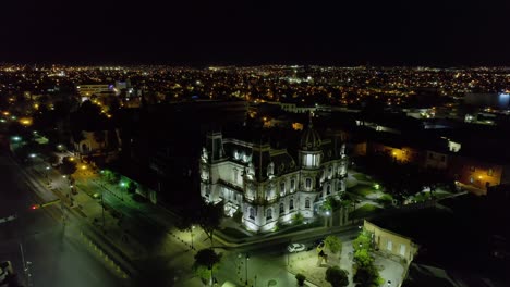 Aerial-view-away-from-the-Illuminated-Quinta-Gameros-building-in-Chihuahua,-night-in-Mexico---reverse,-drone-shot