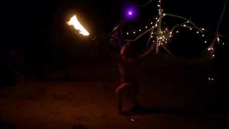 Asian-woman-dressed-in-tribal-attire-dancing-and-spinning-flame-sword-during-fire-ritual-ceremony,-filmed-in-handheld-style