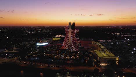 Aerial-view-approaching-the-illuminated-Seminole-Hard-Rock-Hotel-and-Casino-Hollywood,-evening-in-Florida,-USA