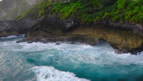 Stunning-cinematic-aerial-view-of-waves-of-the-ocean-crashing-on-the-exotic-green-and-lush-cliffs