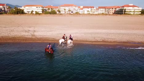 Aerial-orbit-shot-of-Equestrian-riding-horse-on-shoreline-of-Ocean-during-sunset-in-France---Beautiful-mountain-landscape-and-hotel-buildings-at-beach