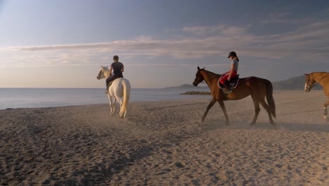 Kamerafahrt-Eines-Magischen-Moments-Am-Strand-Mit-Einer-Gruppe-Von-Pferden,-Die-Gegen-Das-Meer-Und-Das-Sonnenuntergangslicht-Reiten