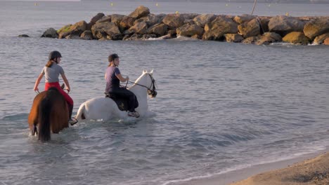 Slow-Motion-shot-of-young-girls-riding-horses-inside-water-shoreline-of-ocean---close-up
