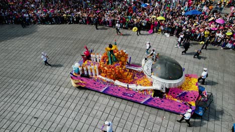 Person-in-costume-standing-on-a-decorated-vehicle,-waving-for-the-crowd-in-Mexico-city-at-the-Dia-de-Muertos-parade---aerial-view