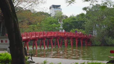 Striking-red-Huc-Bridge-over-Hoan-Kiem-Lake,-pedestrians,-Hanoi