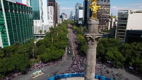 Aerial-view-overlooking-the-Dia-de-Muertos-Parade-behind-the-angel-of-independence-statue,-in-Mexico-city
